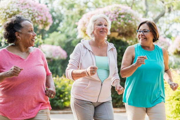 Three Older Women Jogging Together in a Park, Enjoying Their Exercise and the Fresh Air Amidst Greenery.