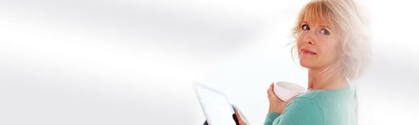 A Woman Sits at a Desk, Holding a Cup of Coffee While Looking at Her Computer Screen.